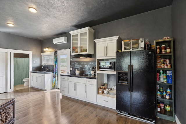 4528 Adellon Ct, Stevensville, MT 59870 - kitchen with black appliances, a wall unit AC, wood finished floors, dark countertops, and a textured ceiling