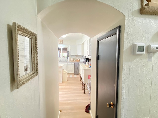 hallway featuring arched walkways, a textured wall, and light wood-style floors