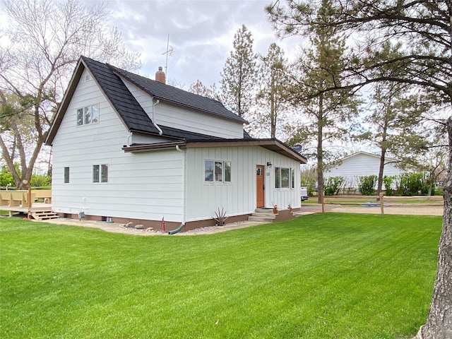 view of side of property with roof with shingles, a deck, a yard, and a chimney