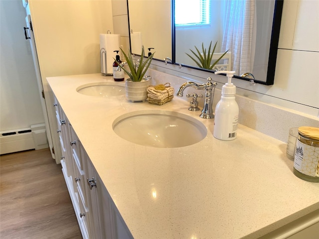 full bathroom featuring double vanity, a sink, a baseboard heating unit, and wood finished floors