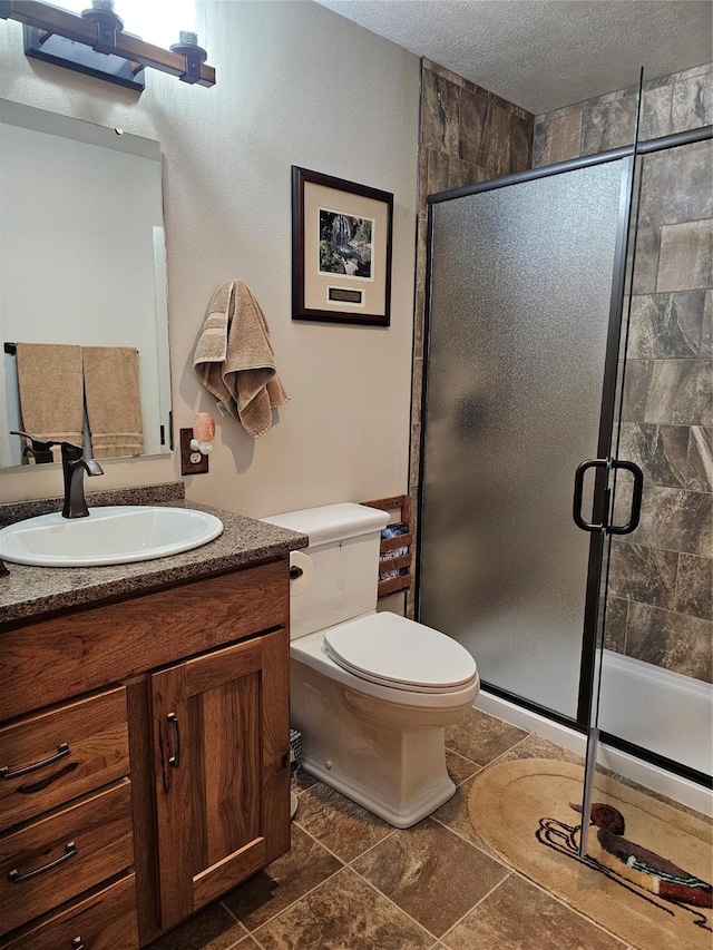 bathroom with a textured ceiling, vanity, toilet, and a stall shower