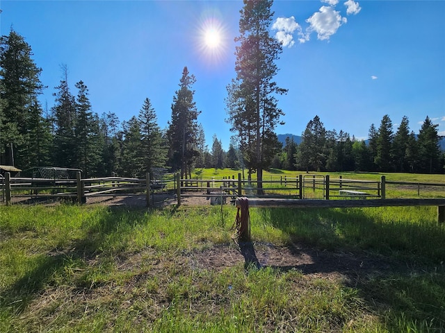 view of yard featuring a wooded view, fence, and a rural view