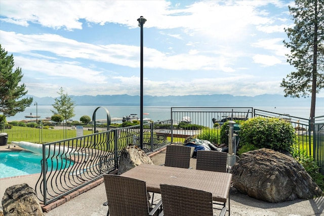 view of patio with fence, a fenced in pool, outdoor dining space, and a water and mountain view
