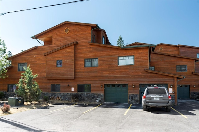 view of front of property featuring a garage, driveway, stone siding, and central AC unit