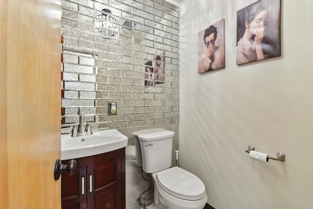 bathroom with toilet, vanity, and brick wall