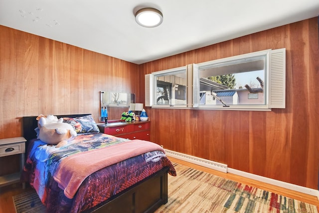 bedroom with wood finished floors, wooden walls, and baseboard heating
