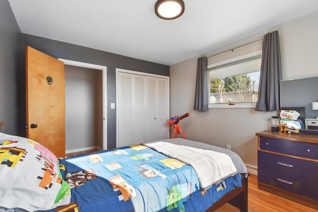 bedroom with a closet, baseboards, light wood-style floors, and a baseboard heating unit