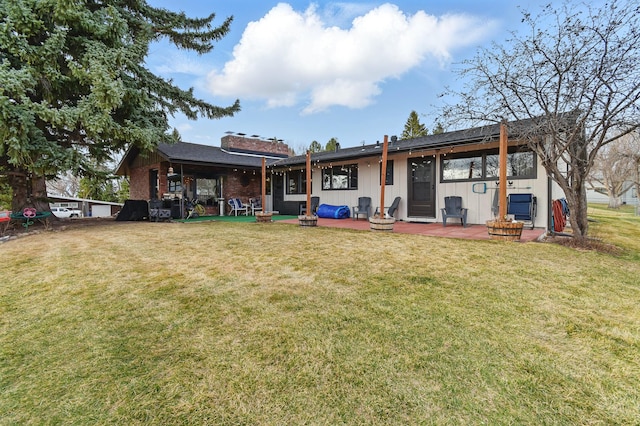 rear view of property with board and batten siding, a lawn, and a patio area