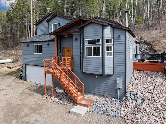 view of front of property featuring a garage, a wooden deck, driveway, and a wooded view