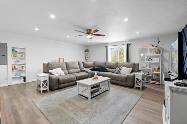 living area with ceiling fan, recessed lighting, electric panel, built in shelves, and light wood finished floors
