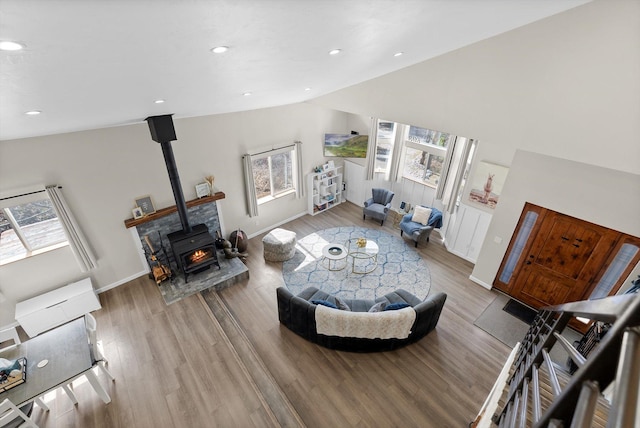 living area featuring baseboards, a wood stove, vaulted ceiling, and wood finished floors