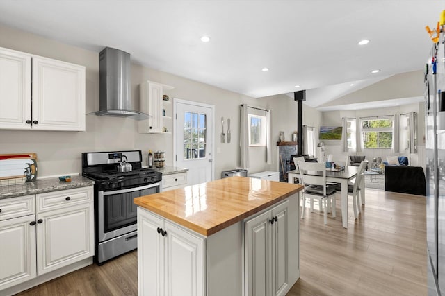 kitchen with stainless steel gas range, a wood stove, wood counters, wall chimney exhaust hood, and open floor plan