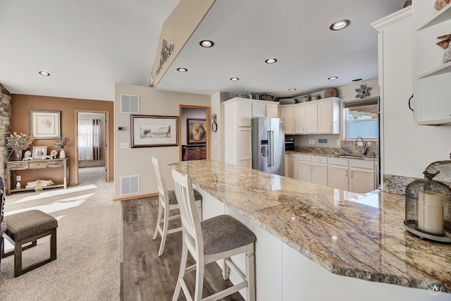 kitchen with visible vents, a peninsula, a healthy amount of sunlight, high end fridge, and light stone countertops
