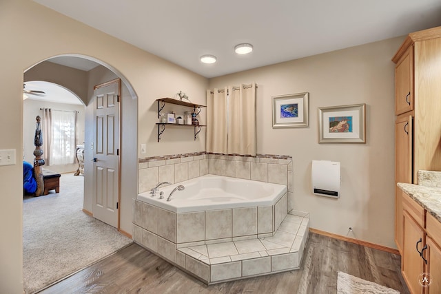 ensuite bathroom with vanity, baseboards, a garden tub, and wood finished floors