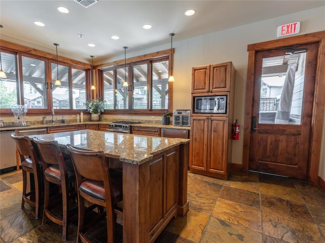 6104 Monterra Ave Unit L, Whitefish, MT 59937 - kitchen with appliances with stainless steel finishes, stone tile floors, recessed lighting, light stone countertops, and a kitchen island