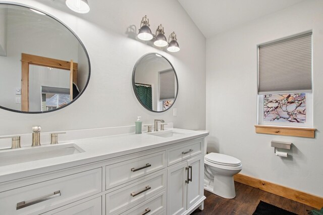 full bath featuring a sink, toilet, double vanity, and wood finished floors