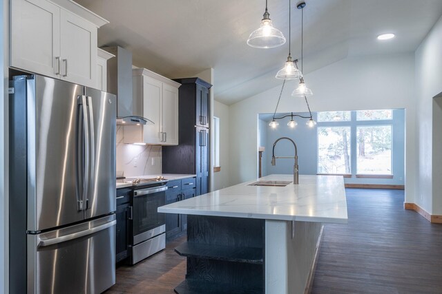 kitchen with wall chimney range hood, white cabinets, appliances with stainless steel finishes, a kitchen island with sink, and a sink