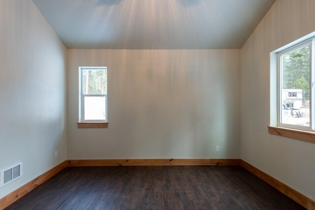empty room with a wealth of natural light, visible vents, dark wood-style flooring, and baseboards