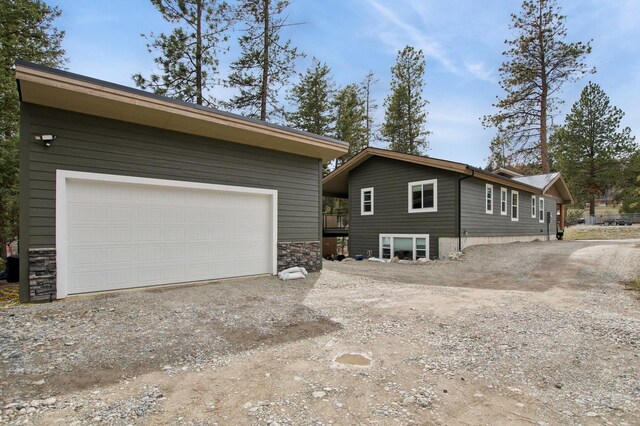 view of property exterior featuring an outdoor structure, stone siding, a garage, and driveway