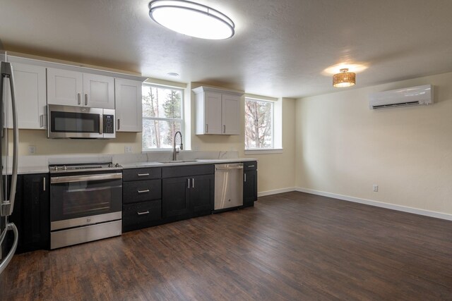 kitchen with a sink, light countertops, appliances with stainless steel finishes, a wall mounted AC, and dark wood-style floors