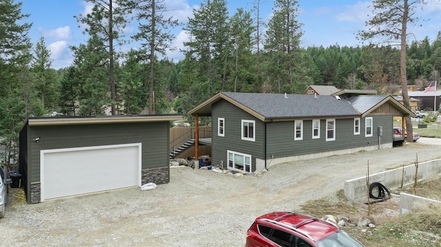 rear view of property featuring a shingled roof, a forest view, an outdoor structure, and a detached garage