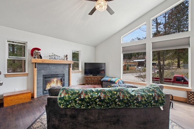 living room with wood finished floors, a tiled fireplace, a ceiling fan, and vaulted ceiling