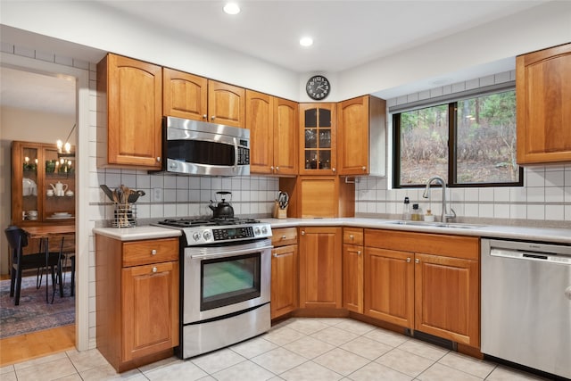 kitchen featuring stainless steel appliances, a sink, light countertops, brown cabinets, and recessed lighting