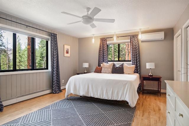 bedroom featuring a wall unit AC, a baseboard heating unit, and light wood-style floors