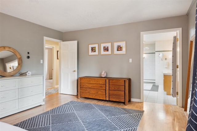 bedroom with light wood finished floors, baseboards, and connected bathroom