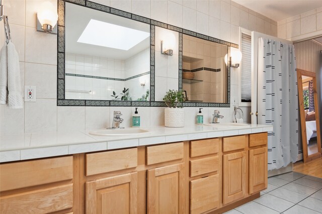 bathroom with a skylight, double vanity, tile patterned flooring, and tasteful backsplash