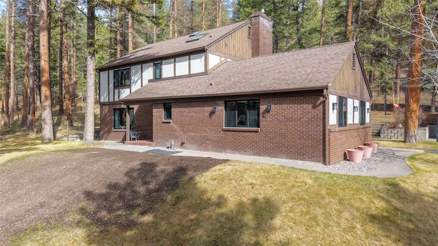 back of house featuring roof with shingles, brick siding, a chimney, and a lawn