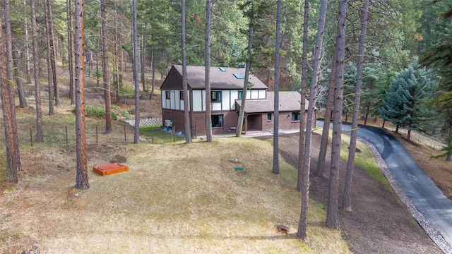 view of front of house featuring driveway, a forest view, a shingled roof, and brick siding