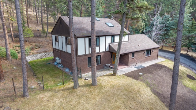 rear view of property featuring roof with shingles, brick siding, a lawn, and driveway