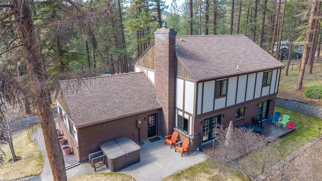 back of property featuring a patio area, a chimney, brick siding, a shingled roof, and board and batten siding