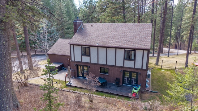 back of house featuring french doors, a chimney, roof with shingles, a deck, and stucco siding