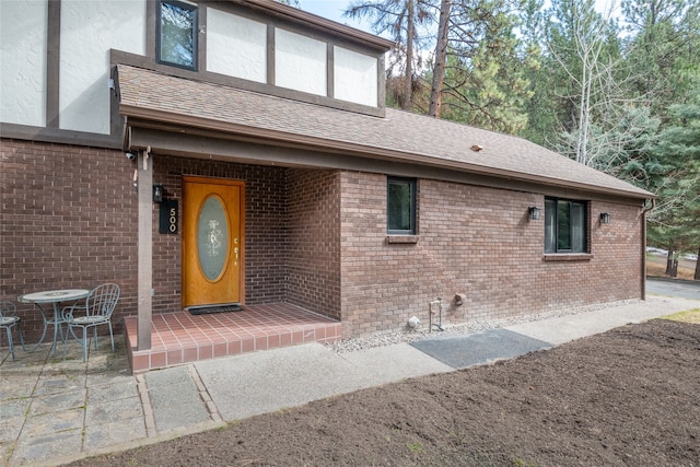 property entrance featuring brick siding and a shingled roof