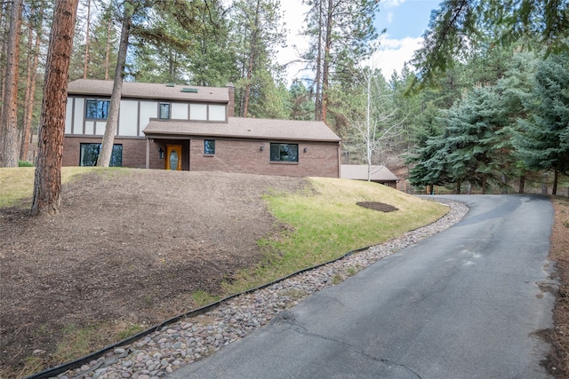 view of front facade with asphalt driveway, brick siding, and a front lawn