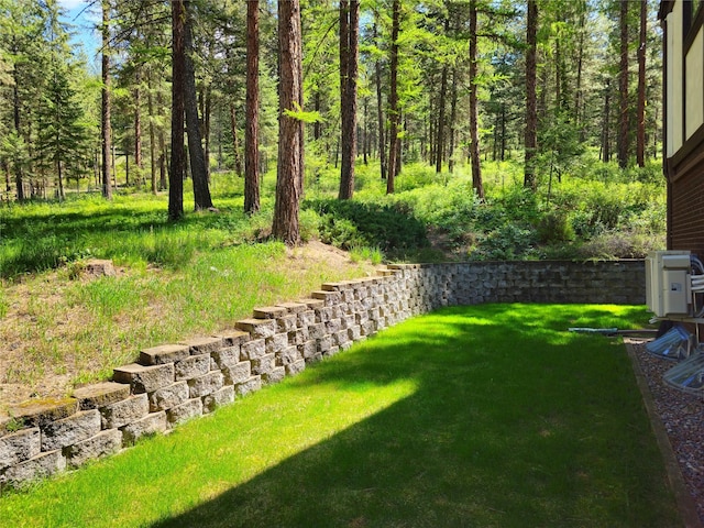 view of green lawn featuring a forest view
