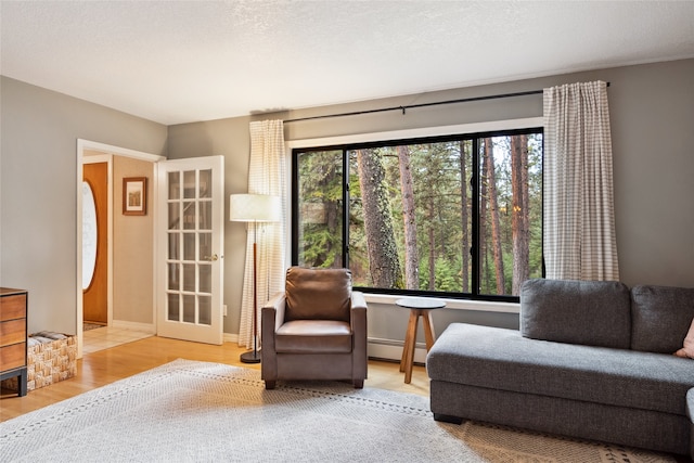 sitting room with healthy amount of natural light, a baseboard heating unit, and wood finished floors
