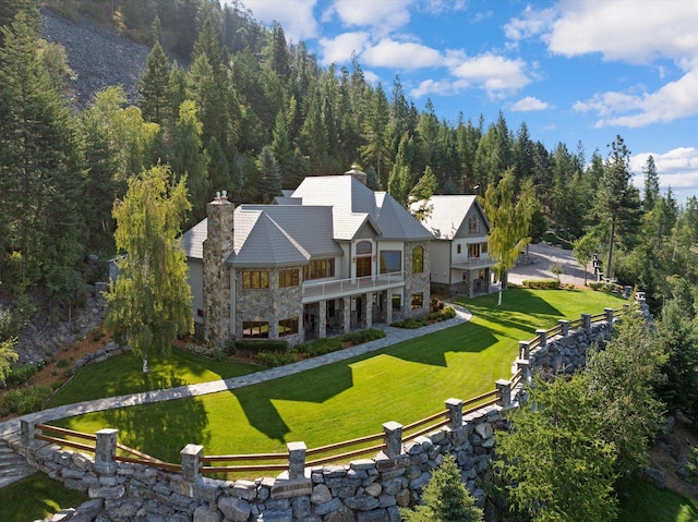 31572 Lake To Sky Dr, Bigfork, MT 59911 - rear view of property featuring a balcony, stone siding, a chimney, a fenced backyard, and a wooded view