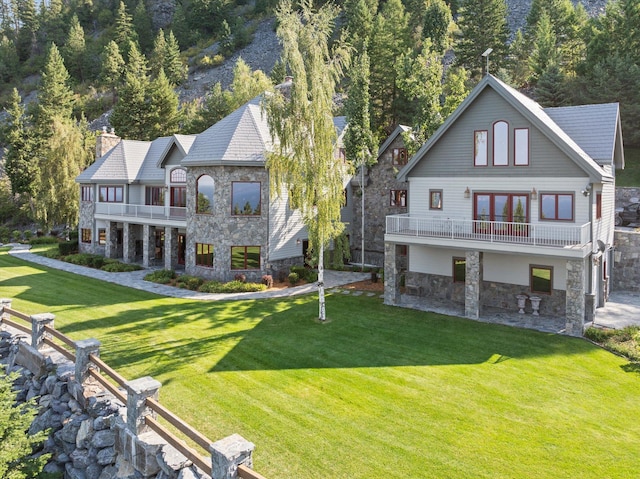 31572 Lake To Sky Dr, Bigfork, MT 59911 - rear view of house featuring stone siding, a balcony, a lawn, and a patio area