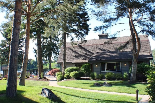 view of front of home featuring roof with shingles, a chimney, and a front yard