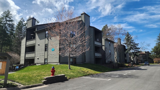 exterior space with uncovered parking, a yard, and a chimney