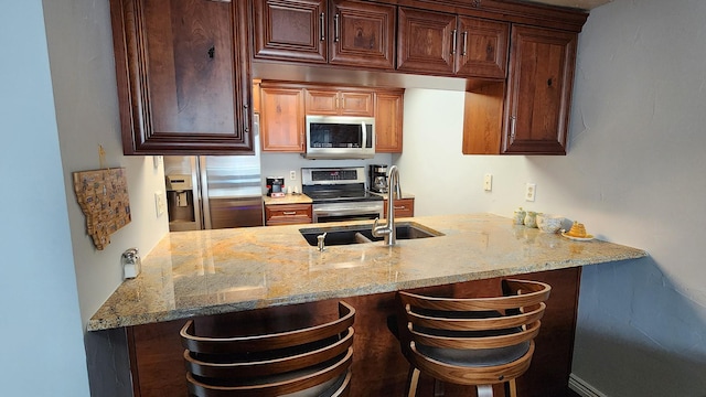 kitchen with a peninsula, a kitchen breakfast bar, light stone counters, a sink, and stainless steel appliances