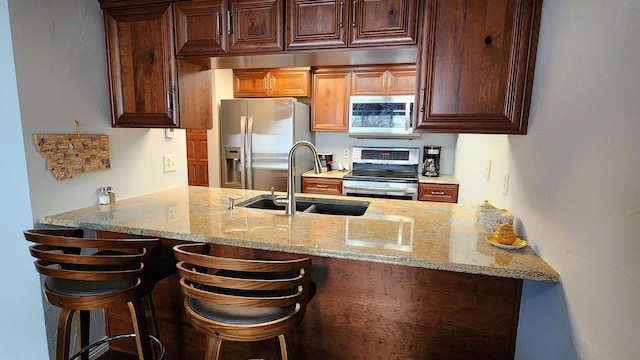 kitchen with a peninsula, a breakfast bar, light stone counters, a sink, and stainless steel appliances