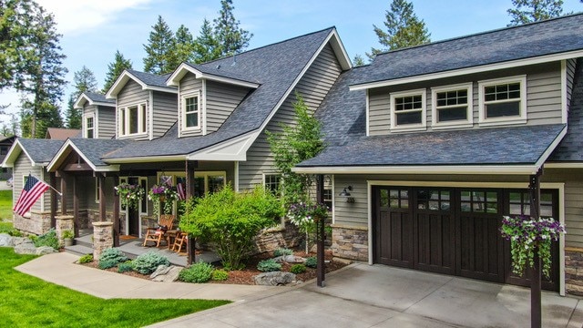 255 Windsor Ct, Bigfork, MT 59911 - view of front of house featuring concrete driveway, stone siding, an attached garage, a shingled roof, and covered porch