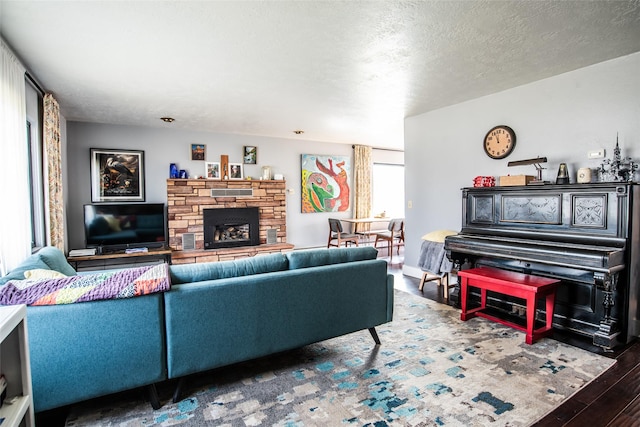 living room featuring wood finished floors, a stone fireplace, and a textured ceiling