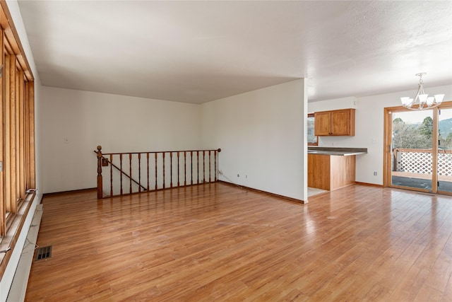 unfurnished living room with light wood-style floors, a notable chandelier, baseboards, and visible vents