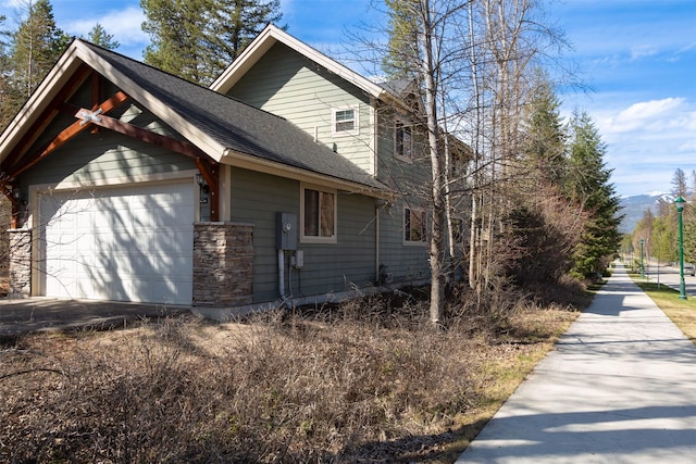 100 Forest Ridge Dr Unit B, Whitefish, MT 59937 - view of side of home featuring roof with shingles, stone siding, a garage, and a mountain view