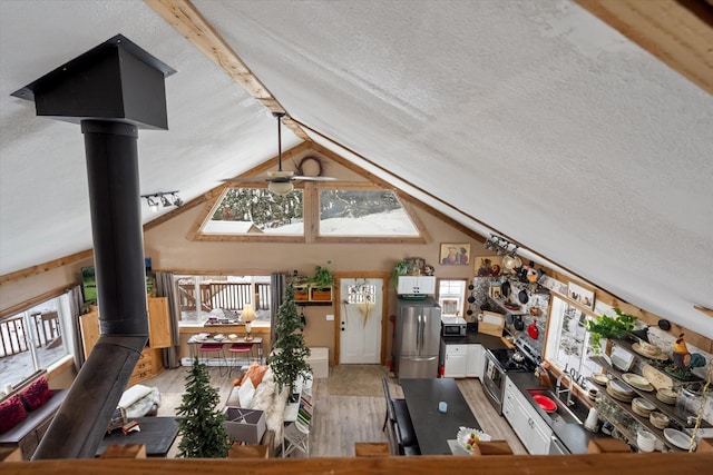 4695 Star Meadow Rd, Whitefish, MT 59937 - living area with light wood finished floors, a ceiling fan, lofted ceiling, a textured ceiling, and a wood stove